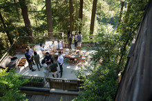Friends Talking Around Long Dining Table On Balcony In Woods At Wedding Reception