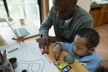 Father And Son Drawing And Playing With Toy Cars On Table