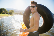 Portrait Young Man Wearing Sunglasses Holding Inner Tube At Sunny Summer Lake