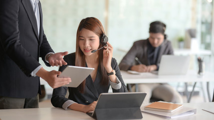 Close up view of customer service  talking on headset while co worker giving her information