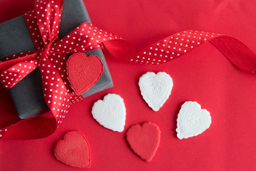 red and white hearts and a gift box with a red ribbon in a white dot on a red background on an abstract background