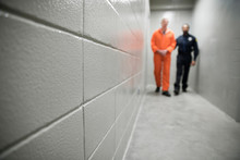 Bailiff Walking Prisoner In Orange Jumpsuit Down Corridor In Jail