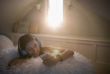 Smiling Teenage Girl Listening To Music With Headphones And Mp3 Player On Fuzzy Bean Bag Chair