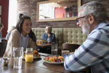 Grandfather And Teenage Granddaughter Talking, Eating Brunch At Diner Table