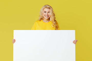 Wall Mural - Young happy woman peeks out from behind a white banner on a yellow background. Point to an empty blank on a form, a copy space for text. Horizontal shot