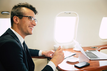 A small talk. Close-up photo of an attractive man in business clothes, who is drinking coffee and having a small talk with his colleague on his business strip, while flying first class.