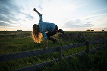 Energetic Young Female Farmer Jumping Over Fence On Farm At Sunset