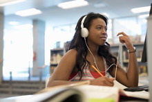 Female College Student With Headphones Studying, Researching In Library