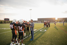 Coach With Clipboard Talking To Teenage Boy High School Football Team On Football Field