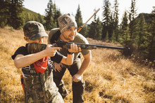 Father Teaching Son With Rifle Hunting In Sunny Field