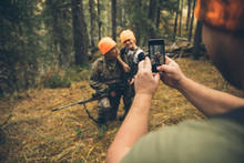 Male Hunter With Camera Phone Photographing Father And Son Hunting In Forest