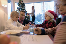 Father Watching Daughters And Son Writing Santa Letters In Christmas Living Room