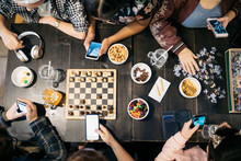 Overhead View Tween Friends Playing Games, Eating Snacks And Texting With Smart Phones At Table