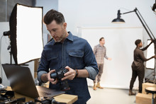 Male Photographer With Digital Camera Using Laptop At Photo Shoot In Studio