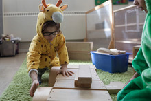Preschool Boy In Giraffe Costume Playing With Wood Blocks In Classroom