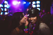 Young Female Millennial Friends Laughing, Sharing Secret In Nightclub