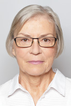 Biometric Passport Photo Of A Senior Woman With Glasses, Neutral Gray Background.