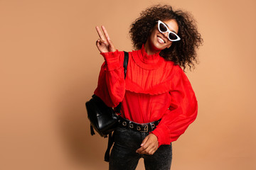 Wall Mural - Blissful young woman with african hairstyle laughing during indoor photoshoot. Fashion girl in romantic red shirt casual clothes enjoying leisure time in studio.Joyful African woman posing in studio 