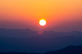 Fototapeta Zachód słońca - Impressive sunrise over forest and hill silhouettes with orange sky.  Amazing beautiful romantic morning and meadow scene.