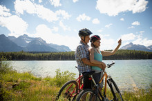 Affectionate Mature Couple Taking Selfie With Camera Phone, Mountain Biking Along Sunny Remote Lake, Alberta, Canada