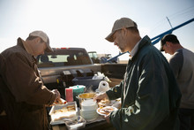 Male Farmers Eating Lunch At Pickup Truck On Sunny Farm