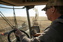 Male Farmer Driving Combine Harvester In Sunny Field