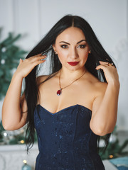 Canvas Print - Portrait of a girl with black hair in a blue dress on a background of Christmas decorations.