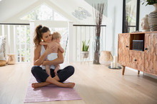 Affectionate Mother Holding Baby Daughter On Yoga Mat