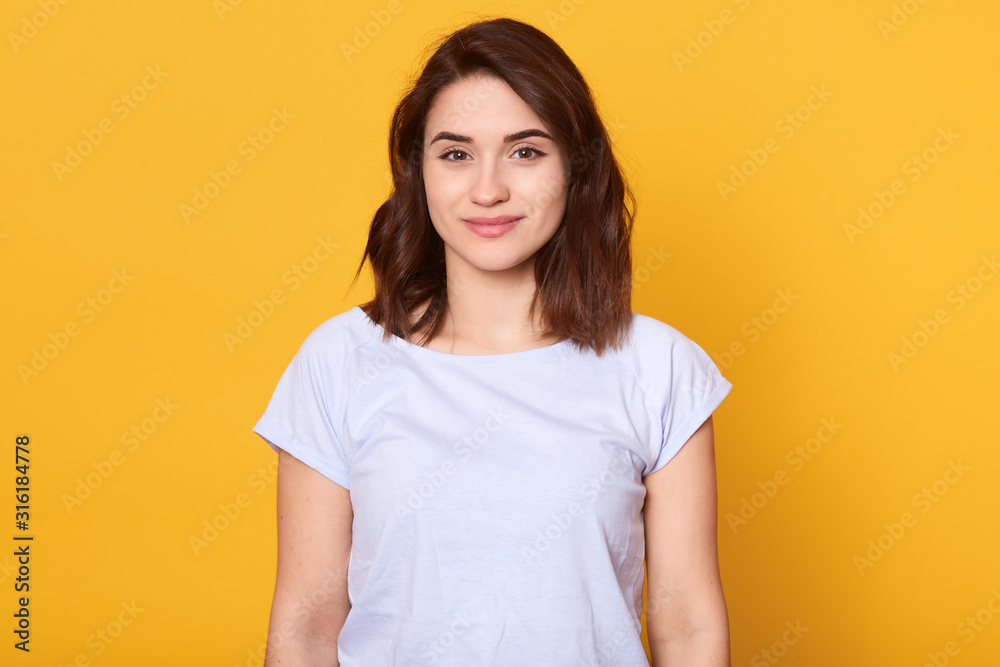 Studio portrait of beautiful young woman with dark hair. Pretty model girl with perfect fresh clean skin looking directly at camera with charming smile, slim female having happy facial expression. - obrazy, fototapety, plakaty 