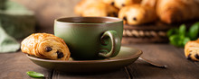 Green Cup Of Tea With Mini Chocolate Bun, Puff Pastry On Old Wooden Table. Tasty Tea Break Concept, Banner.