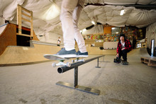 Young Male Skateboarder Sliding On Rail At Indoor Skate Park