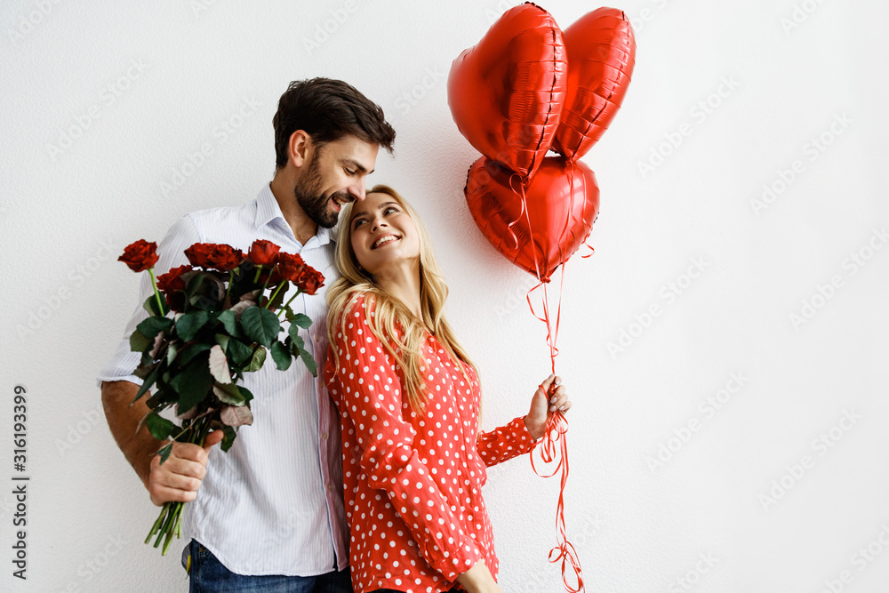 Couple. Love. Valentine's day. Emotions. Man is giving heart-shaped balloons to his woman, both smiling; on a white background - obrazy, fototapety, plakaty 