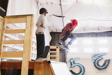 Boy Watching Father Jumping Above Ramp At Indoor Skate Park