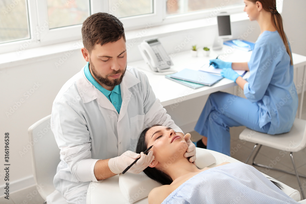 Plastic surgeon applying marks on patient's face in clinic