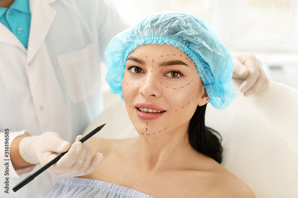Plastic surgeon applying marks on patient's face in clinic