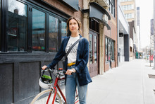 Confident Woman Walking With Bicycle On Urban Sidewalk