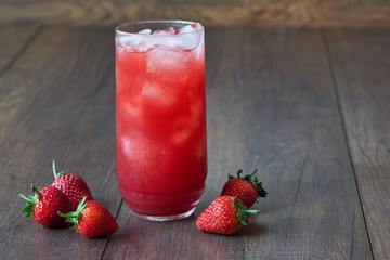 A glass of tasty cold strawberry juice with ice on the table.