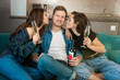 © studioprodakshn - three young friends two beautiful women kissing on the cheek their handsome man friend drinking champagne on the sofa looking happy, celebrating friendship