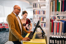 Librarian Assisting Student On Computer In University Library