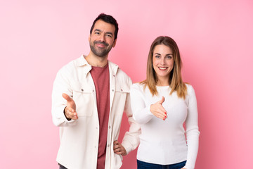 Wall Mural - Couple in Valentine Day over isolated pink background shaking hands for closing a good deal