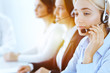 © rogerphoto - Group of diverse phone operators at work in sunny office. Handsome business woman with headphones consulting clients. Call center and business people concept