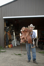 Mature Man Carrying Saddle Outside Barn