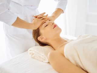 Beautiful woman enjoying facial massage with closed eyes in spa center. Relaxing treatment concept in medicine