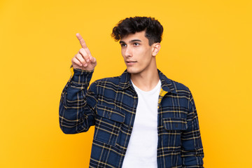 Young Argentinian man over isolated yellow background touching on transparent screen