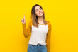 © luismolinero - Pretty young woman over isolated yellow wall showing and lifting a finger in sign of the best