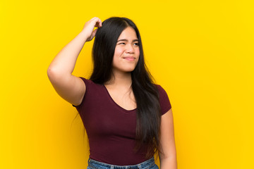 Wall Mural - Young teenager Asian girl over isolated yellow background having doubts and with confuse face expression