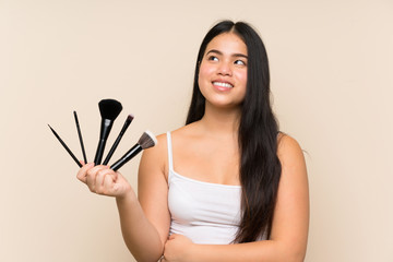 Wall Mural - Young teenager Asian girl holding a lot of makeup brush looking up while smiling