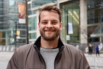 Man with a beard smiling in downtown Toronto with sky rise buildings in the background