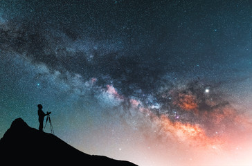 Wall Mural - beautiful starry night landscape. a silhouette of a photographer stands on a hill and looks at a bea