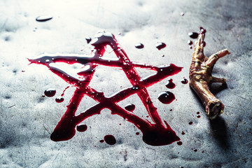 Pentagram drawn from blood on metal table with crow's paw